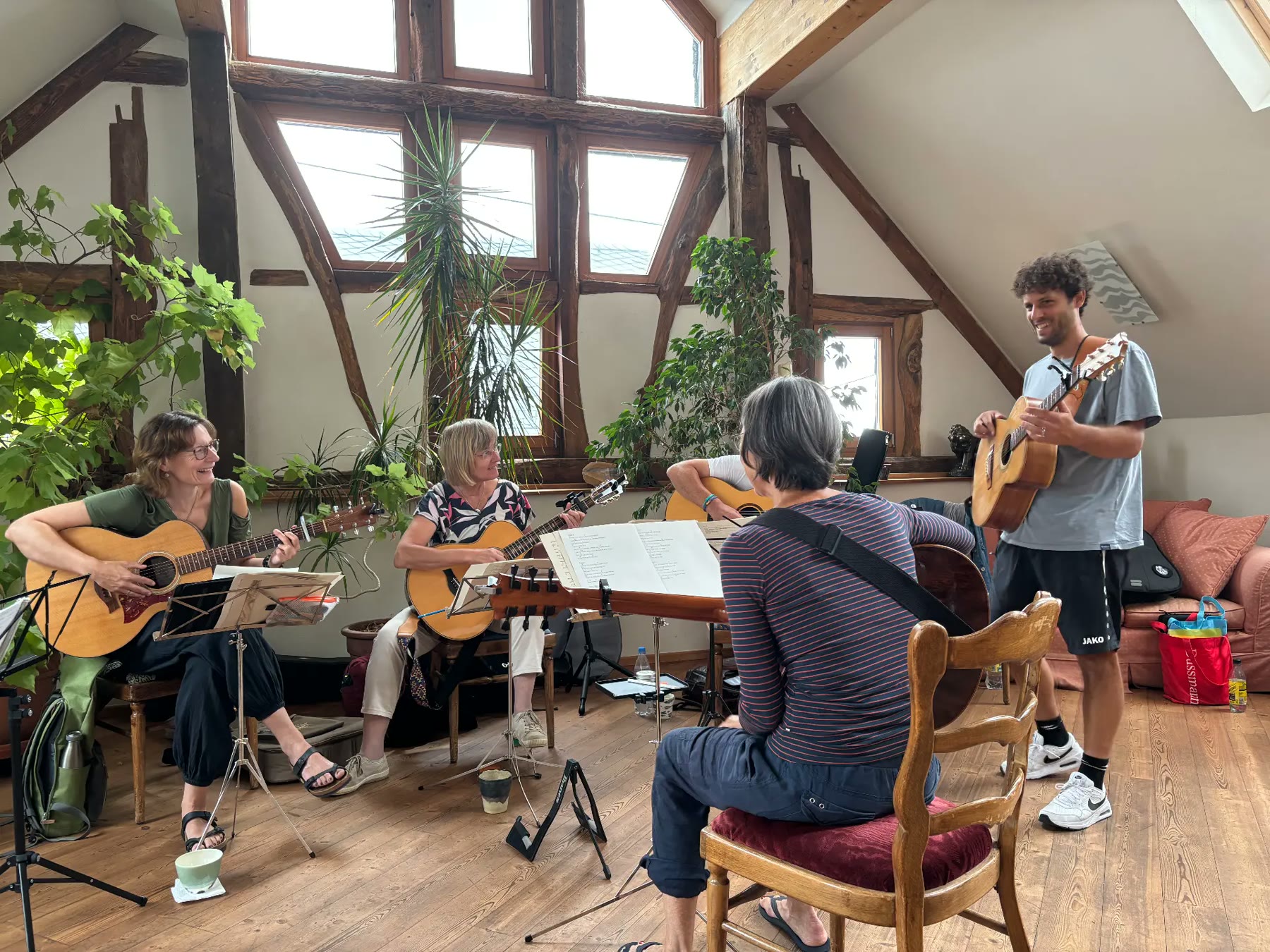 Kleine Gruppe spielt lachend Gitarre in einem Dachraum voller Pflanzen