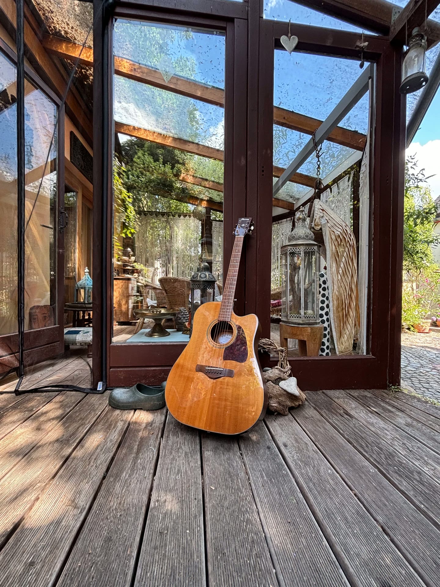 Akustikgitarre lehnt an einer Glastür auf einer Holzveranda